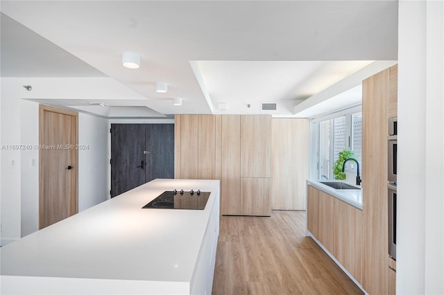 kitchen with black electric cooktop, light hardwood / wood-style floors, a kitchen island, and sink