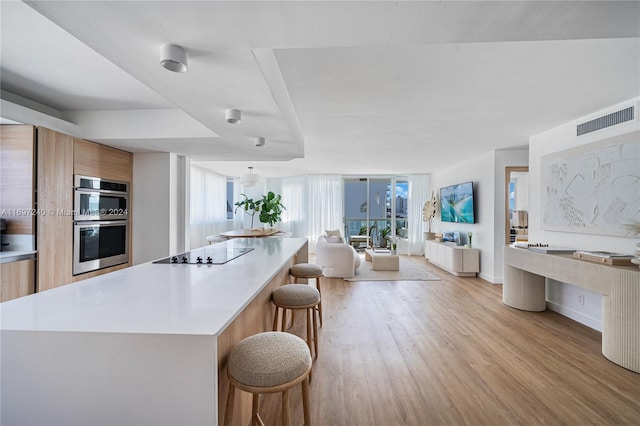 kitchen featuring a center island, stainless steel double oven, black electric cooktop, a breakfast bar, and light wood-type flooring