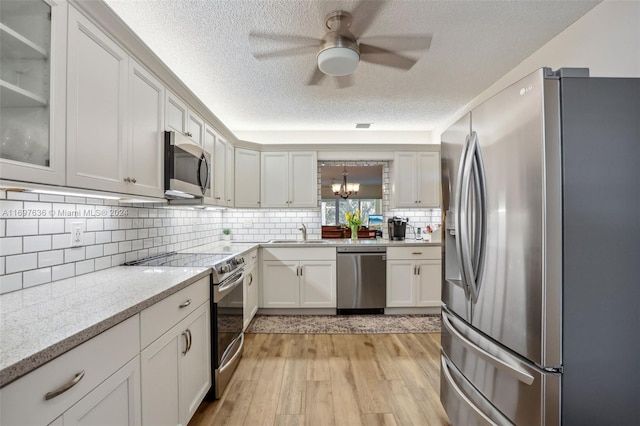 kitchen with light stone countertops, sink, stainless steel appliances, a textured ceiling, and light wood-type flooring