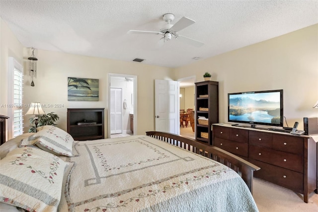 bedroom featuring ceiling fan, ensuite bathroom, a textured ceiling, and light carpet