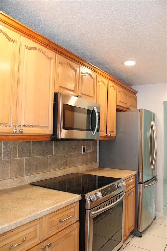 kitchen featuring backsplash, light tile patterned floors, stainless steel appliances, and a textured ceiling