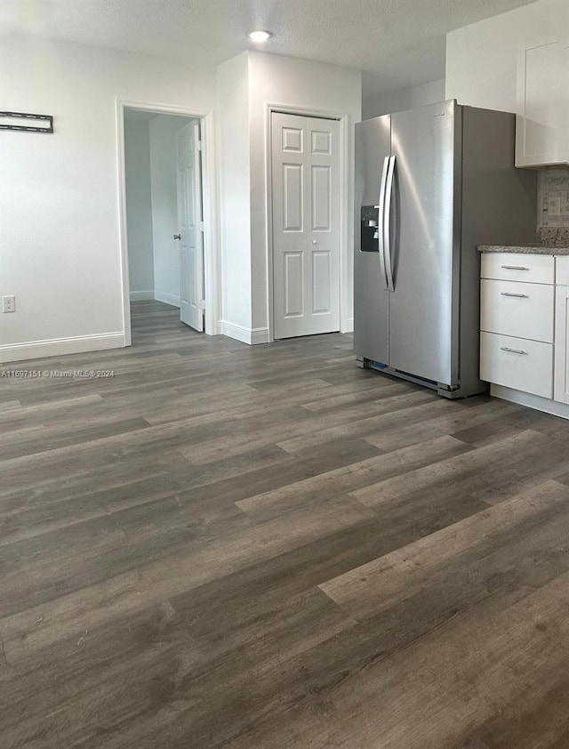 interior space with light stone countertops, stainless steel refrigerator with ice dispenser, a textured ceiling, dark hardwood / wood-style floors, and white cabinetry