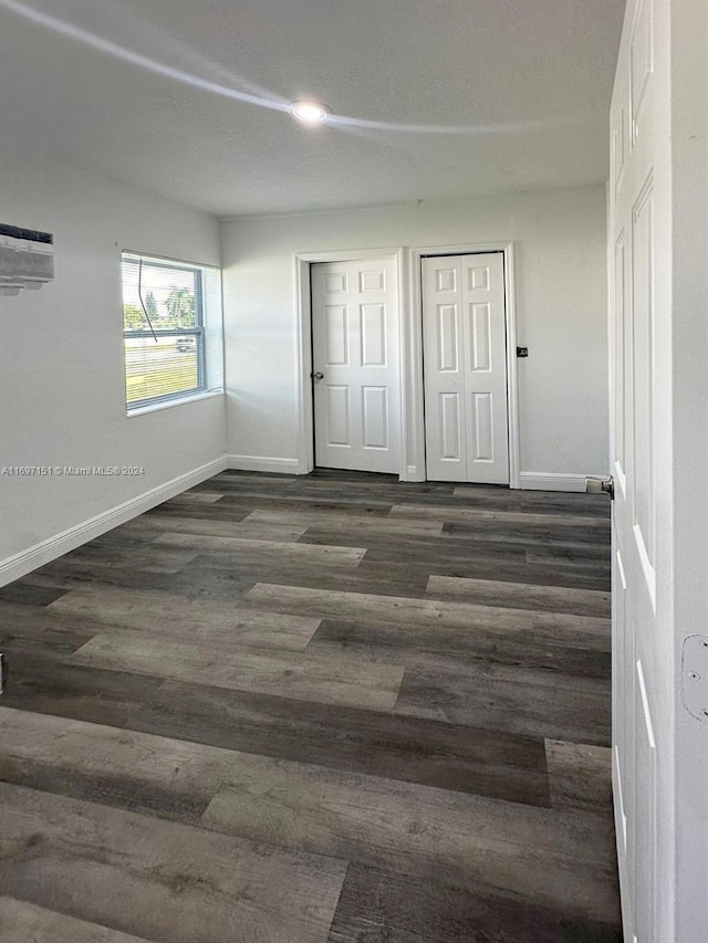 unfurnished bedroom featuring an AC wall unit and dark hardwood / wood-style floors