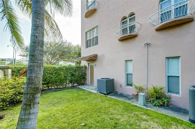 rear view of property featuring a yard, central AC, and a balcony