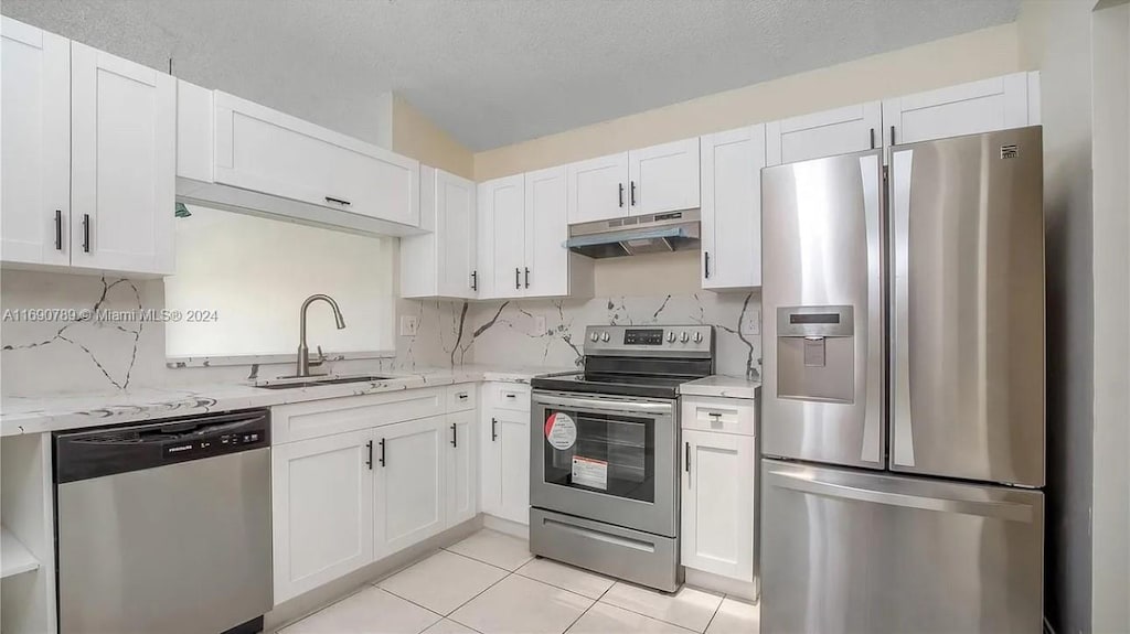 kitchen featuring sink, appliances with stainless steel finishes, tasteful backsplash, light tile patterned flooring, and white cabinetry