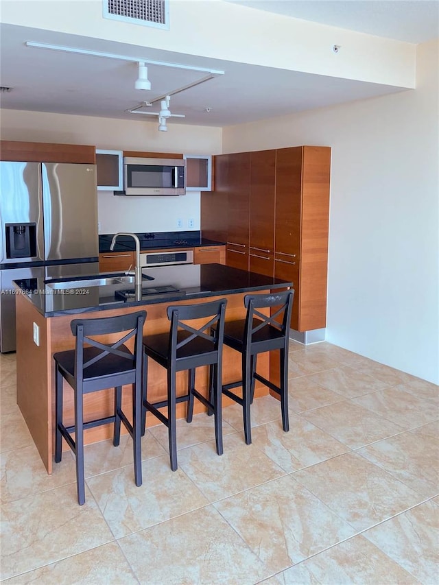 kitchen featuring a kitchen breakfast bar, light tile patterned floors, an island with sink, and appliances with stainless steel finishes