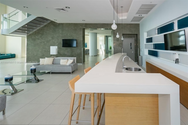 kitchen featuring sink, light tile patterned floors, an island with sink, decorative light fixtures, and a breakfast bar area