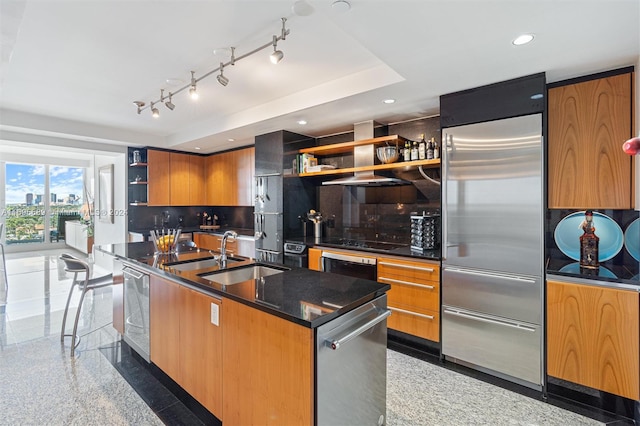 kitchen featuring decorative backsplash, a kitchen island with sink, sink, built in fridge, and black stovetop