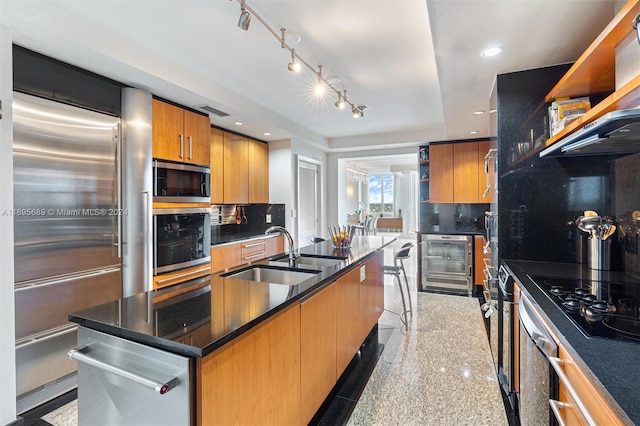 kitchen featuring decorative backsplash, appliances with stainless steel finishes, a kitchen island with sink, beverage cooler, and sink