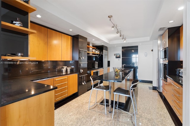 kitchen featuring a raised ceiling, tasteful backsplash, a kitchen bar, a kitchen island, and appliances with stainless steel finishes