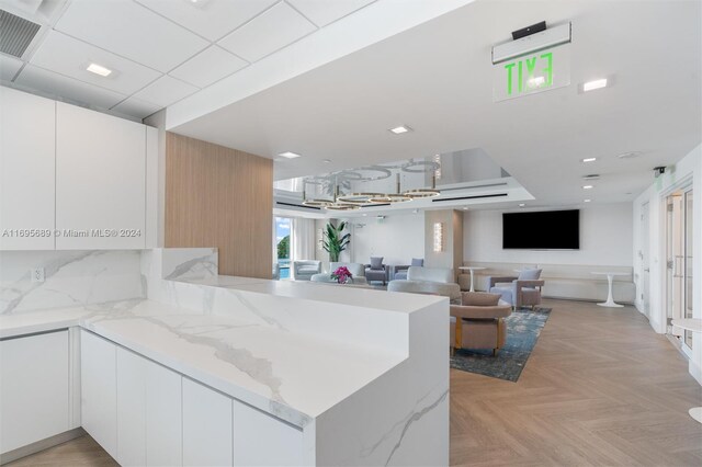 kitchen with white cabinets, light stone countertops, kitchen peninsula, and light parquet flooring