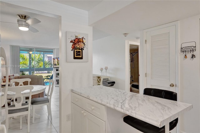 kitchen featuring ceiling fan, white cabinets, light tile patterned flooring, and light stone counters