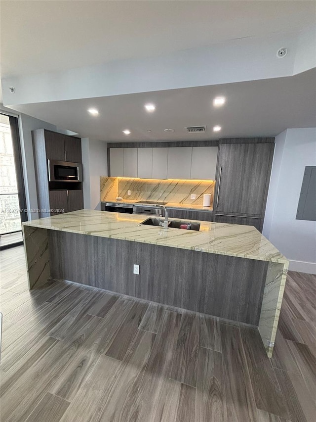 kitchen featuring light stone countertops, sink, a baseboard radiator, tasteful backsplash, and hardwood / wood-style flooring