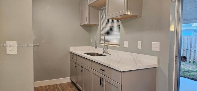 kitchen featuring gray cabinetry, dark wood-type flooring, a sink, baseboards, and light stone countertops