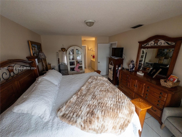 bedroom featuring ensuite bath, light tile patterned floors, and a textured ceiling