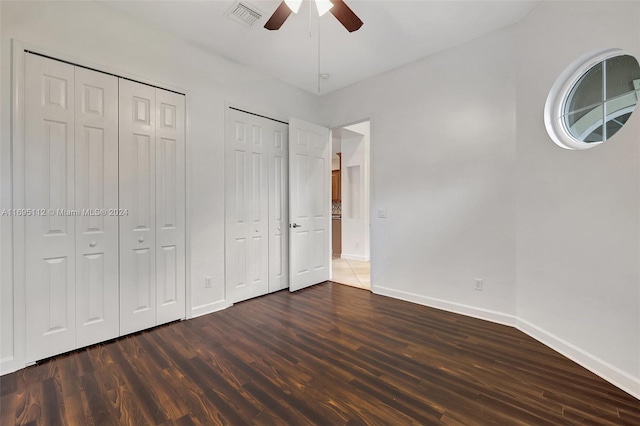 unfurnished bedroom with ceiling fan, dark wood-type flooring, and multiple closets