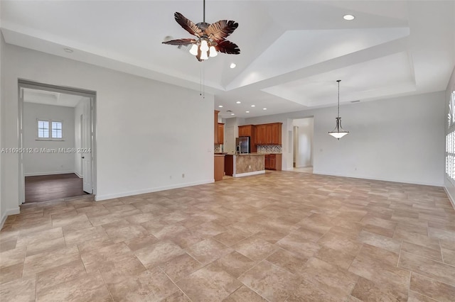 unfurnished living room with ceiling fan, a raised ceiling, and vaulted ceiling