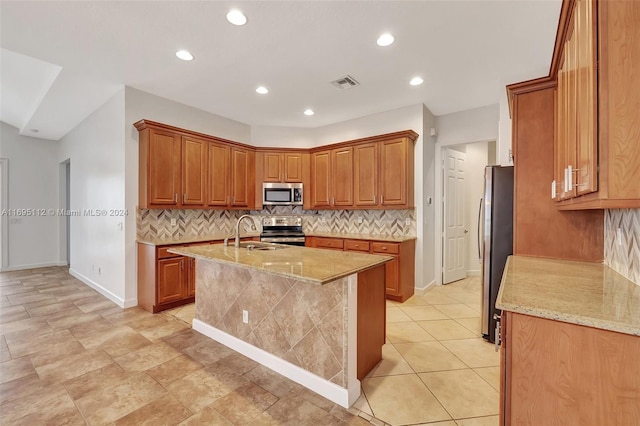 kitchen featuring light stone countertops, appliances with stainless steel finishes, backsplash, sink, and an island with sink