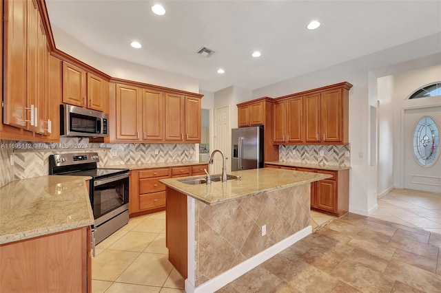 kitchen featuring light stone countertops, sink, backsplash, a center island with sink, and appliances with stainless steel finishes