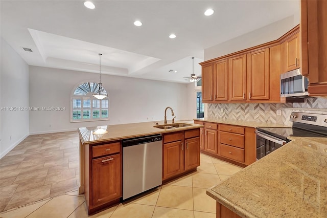 kitchen with tasteful backsplash, stainless steel appliances, sink, hanging light fixtures, and an island with sink