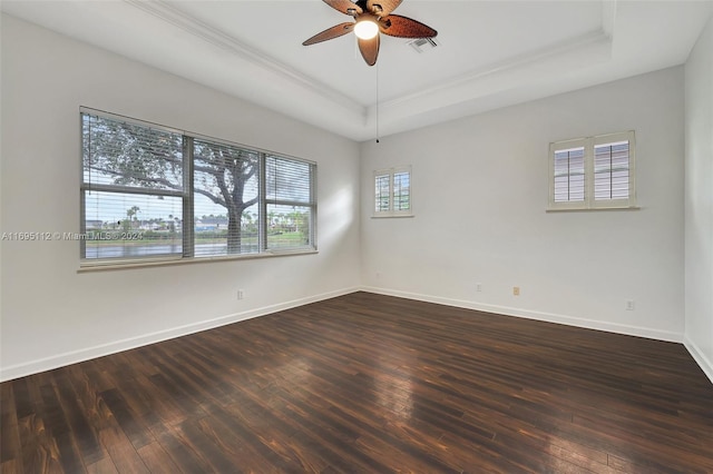 empty room featuring a tray ceiling, ceiling fan, dark wood-type flooring, and a healthy amount of sunlight