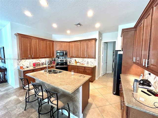 kitchen with a kitchen bar, appliances with stainless steel finishes, a textured ceiling, and a center island with sink