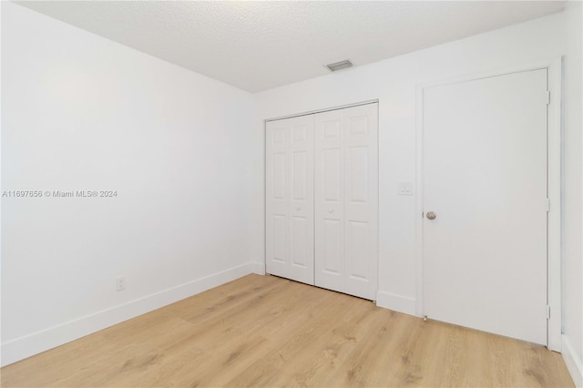 unfurnished bedroom with a closet, a textured ceiling, and light hardwood / wood-style flooring