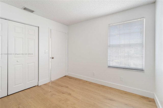 unfurnished bedroom with light hardwood / wood-style floors, a textured ceiling, and a closet