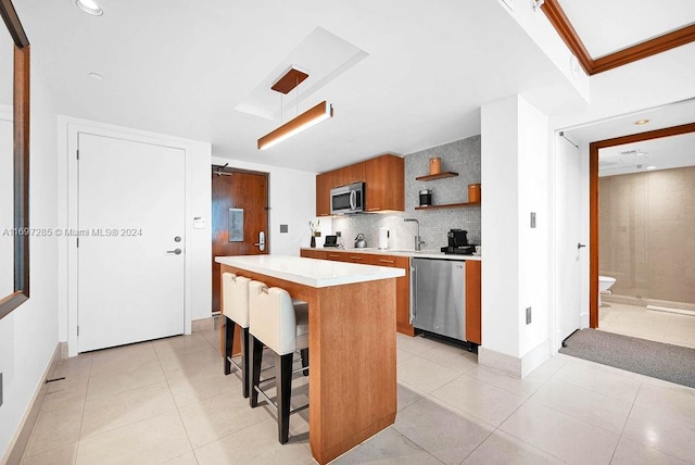 kitchen with a center island, backsplash, light tile patterned floors, appliances with stainless steel finishes, and a kitchen bar