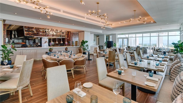 dining area featuring a raised ceiling, floor to ceiling windows, wood-type flooring, and an inviting chandelier