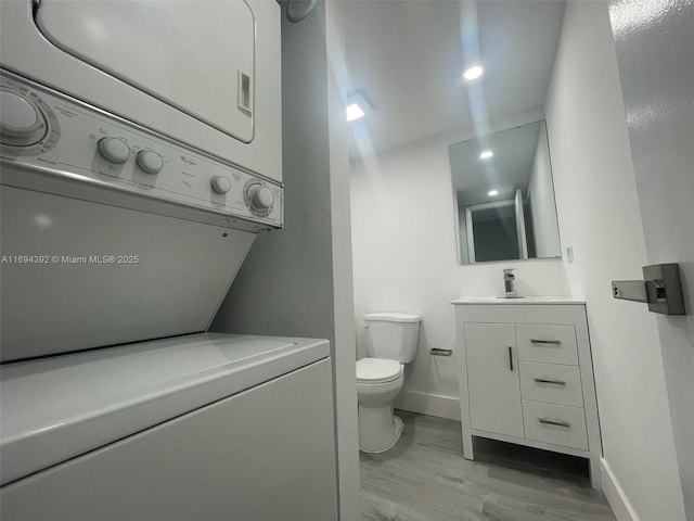 bathroom featuring hardwood / wood-style floors, vanity, toilet, and stacked washer and dryer