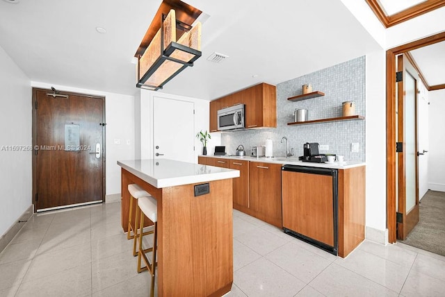 kitchen with decorative backsplash, dishwashing machine, a breakfast bar, light tile patterned floors, and a kitchen island