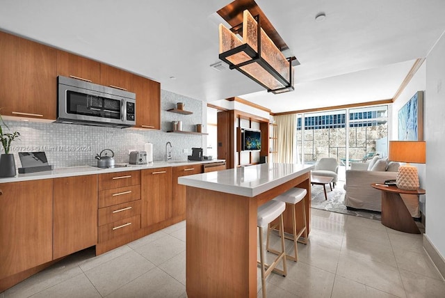 kitchen with decorative backsplash, a kitchen bar, sink, light tile patterned floors, and a center island