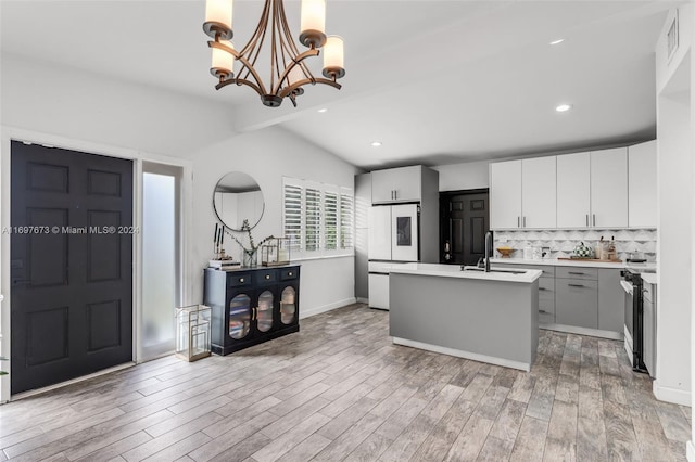 kitchen with hardwood / wood-style floors, a kitchen island with sink, sink, vaulted ceiling, and decorative light fixtures