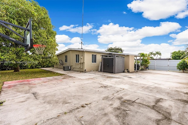 back of property with a yard, a storage unit, central air condition unit, basketball hoop, and a patio