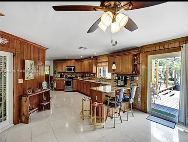 kitchen featuring a breakfast bar, hanging light fixtures, wooden walls, light tile patterned floors, and stainless steel appliances