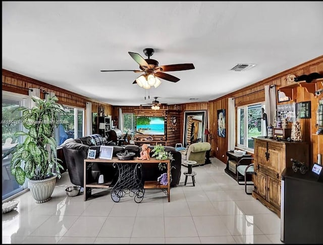 tiled living room with a wealth of natural light, wooden walls, ceiling fan, and crown molding