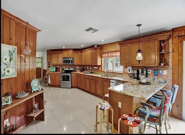 kitchen featuring kitchen peninsula, a kitchen bar, stainless steel appliances, pendant lighting, and wood walls