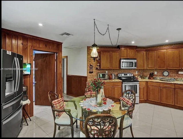 kitchen featuring pendant lighting, backsplash, light stone countertops, light tile patterned floors, and stainless steel appliances