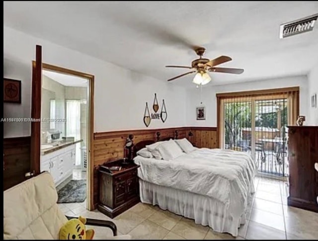 bedroom with ensuite bathroom, access to outside, ceiling fan, light tile patterned floors, and wood walls