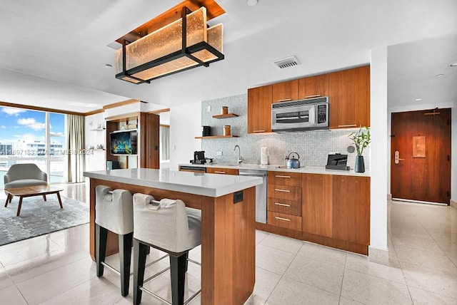 kitchen with decorative backsplash, light tile patterned floors, appliances with stainless steel finishes, a kitchen island, and a kitchen bar