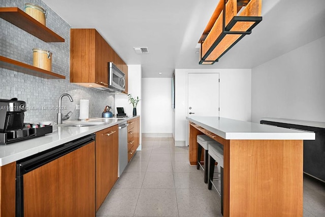 kitchen with sink, stainless steel appliances, light tile patterned floors, backsplash, and a kitchen island