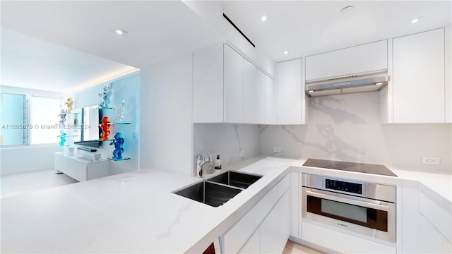 kitchen featuring black electric stovetop, oven, white cabinets, sink, and range hood