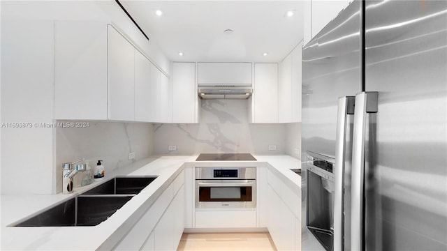 kitchen featuring backsplash, exhaust hood, sink, appliances with stainless steel finishes, and white cabinetry