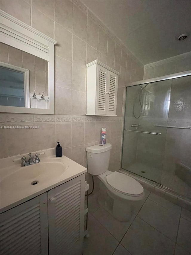 bathroom featuring tile patterned flooring, vanity, a shower with shower door, and tile walls