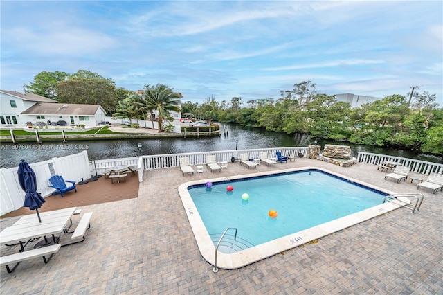 pool with a patio area, a water view, and fence