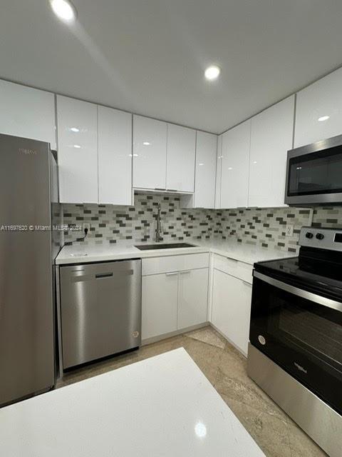 kitchen with backsplash, stainless steel appliances, white cabinetry, and sink