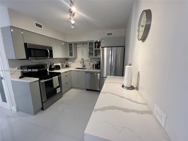 kitchen featuring appliances with stainless steel finishes, light stone counters, sink, light tile patterned floors, and gray cabinets