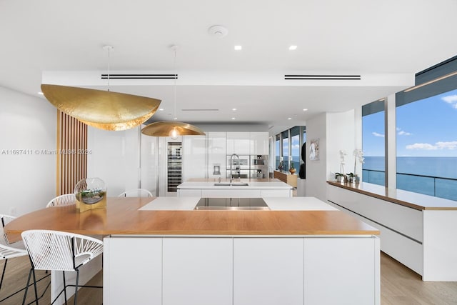 kitchen featuring light wood-type flooring, black electric cooktop, pendant lighting, a water view, and white cabinets