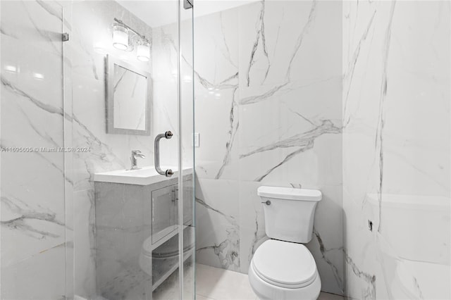 bathroom featuring a shower with door, vanity, tile walls, and toilet